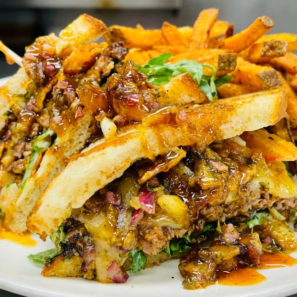 Loaded sandwich topped with saucy ground meat, melted cheese, vegetables, and sweet potato fries on a white plate.