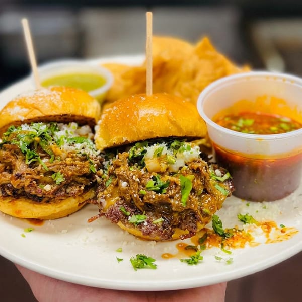 Two saucy sliders topped with pulled meat, herbs, and cheese served with tortilla chips, salsa, and green sauce.