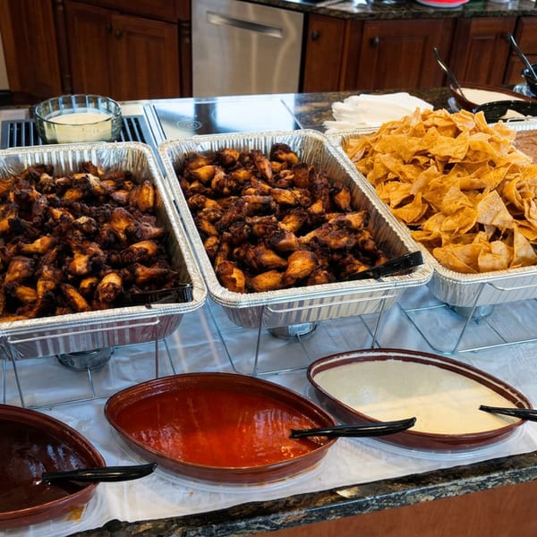 Buffet spread featuring cheesy casseroles, roasted vegetables, tortilla chips, beans, sauces, and creamy dips in serving trays.